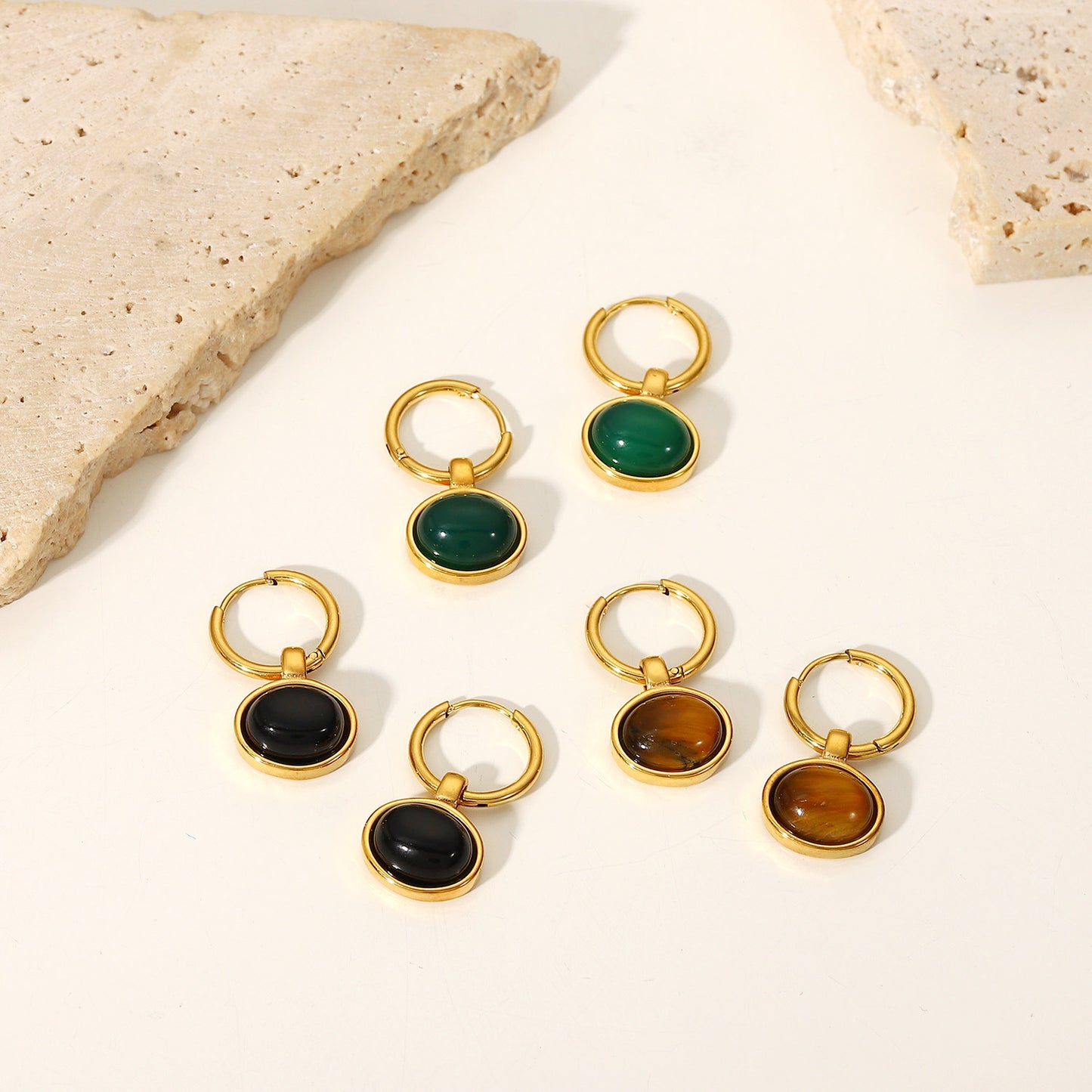 Set of gold hoop earrings with green, black, and brown gemstones on a neutral background