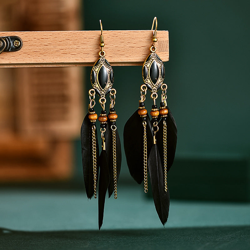 Pair of black feather earrings with gold chains on a wooden stand against a green background from Nested Wisdom