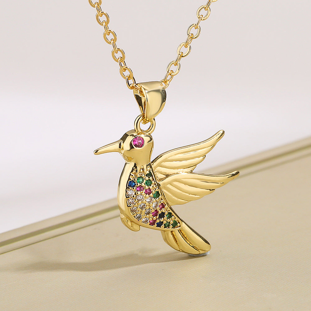 Gold hummingbird pendant with colorful gemstones on a gold chain against a light background