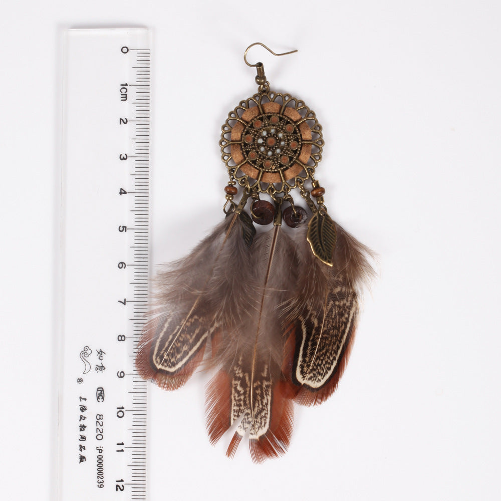 Feathered earrings with decorative elements next to a ruler for scale on a white background