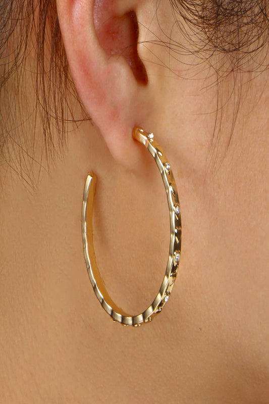 Gold hoop earring worn on an ear with a plain background