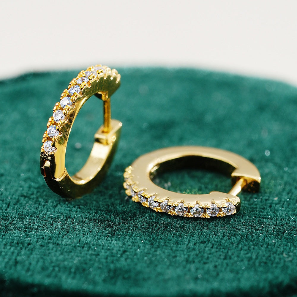 Gold hoop earrings with embedded stones on a green velvet surface