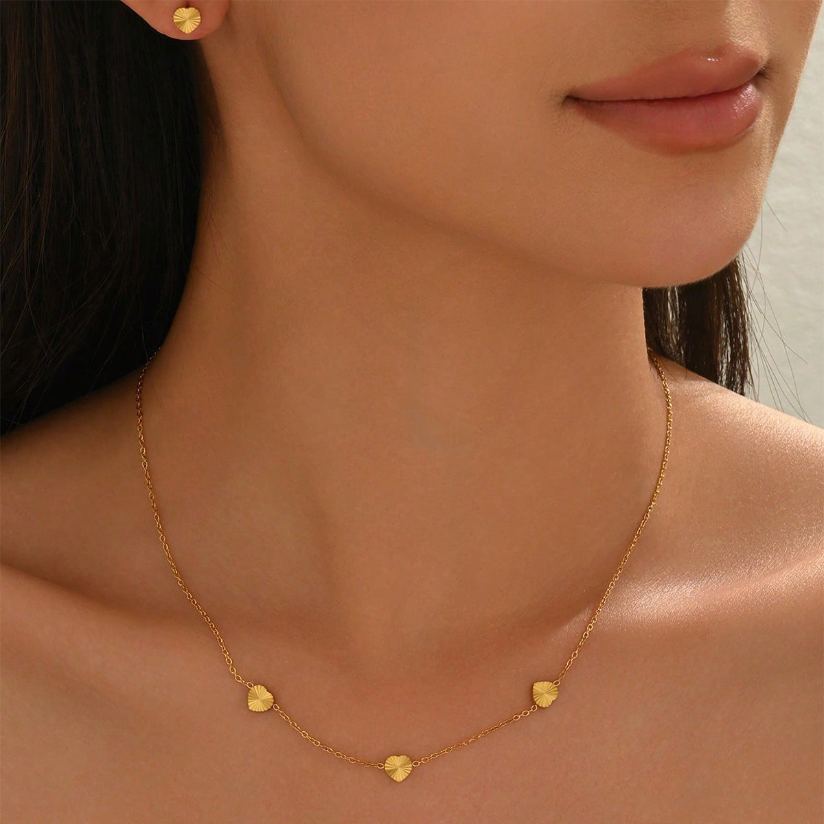 Close-up of a person wearing a gold necklace with heart-shaped pendants.