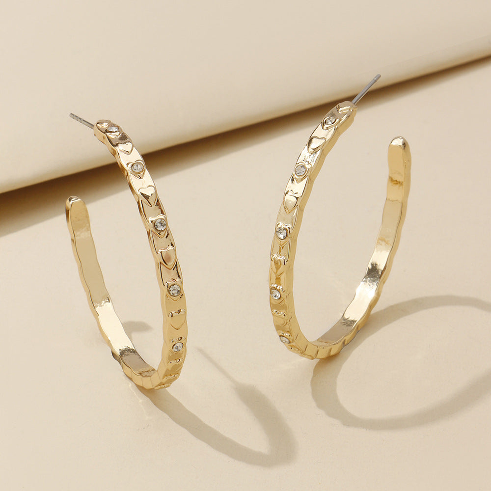 Gold hoop earrings with diamond-like stones on a beige background