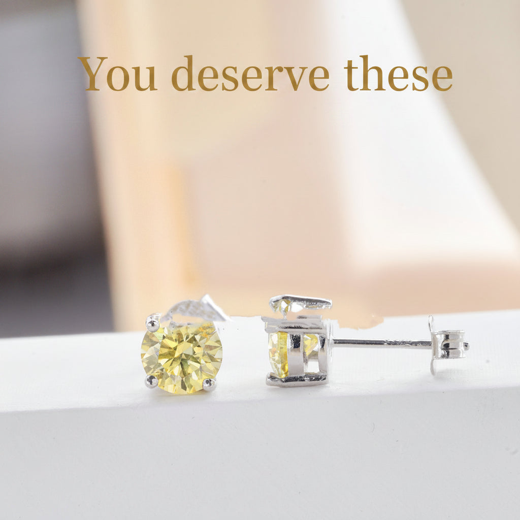 Pair of yellow gemstone stud earrings on a white surface with a soft blurred background