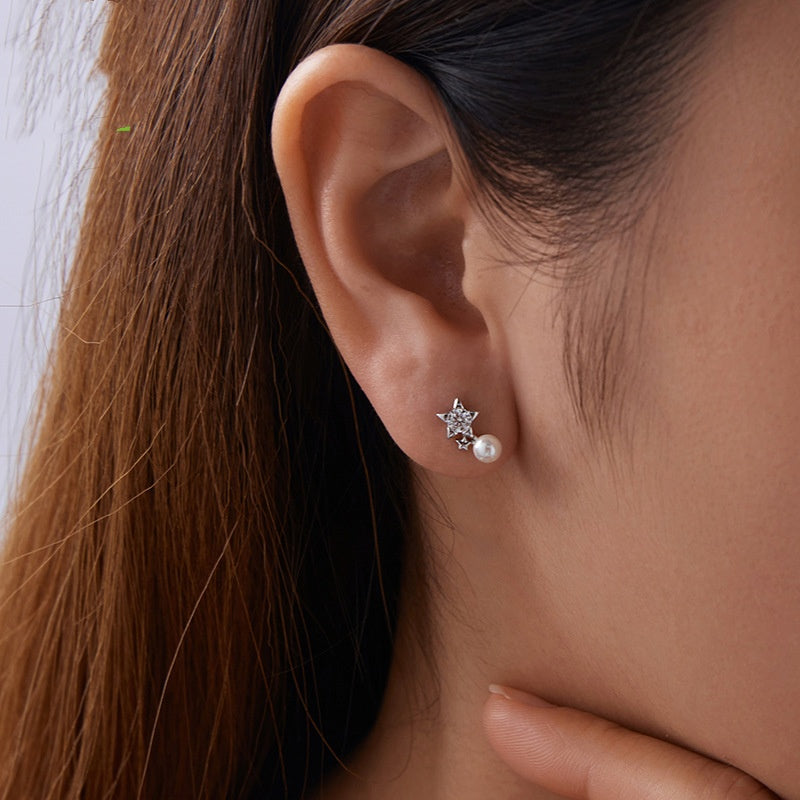 Close-up of an ear wearing a star-shaped earring with a pearl detail.
