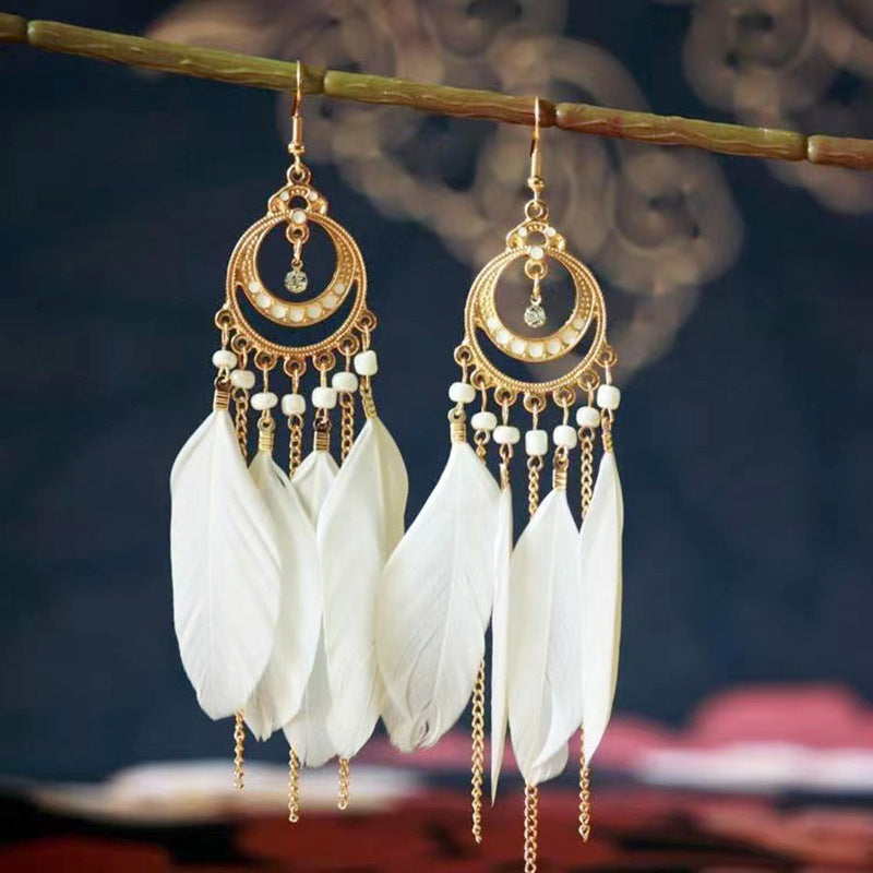 Gold and white feather earrings hanging from a branch with a blurred background