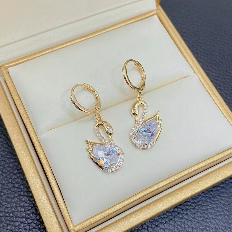 Gold Swan-shaped earrings with crystal details on a gold box.
