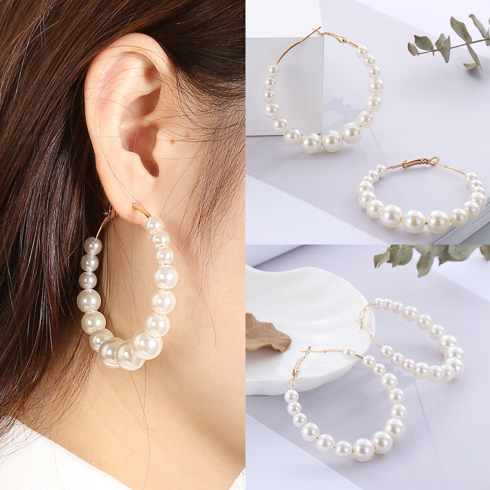 Pearl hoop earrings worn by a person and displayed on a white surface with leaves.