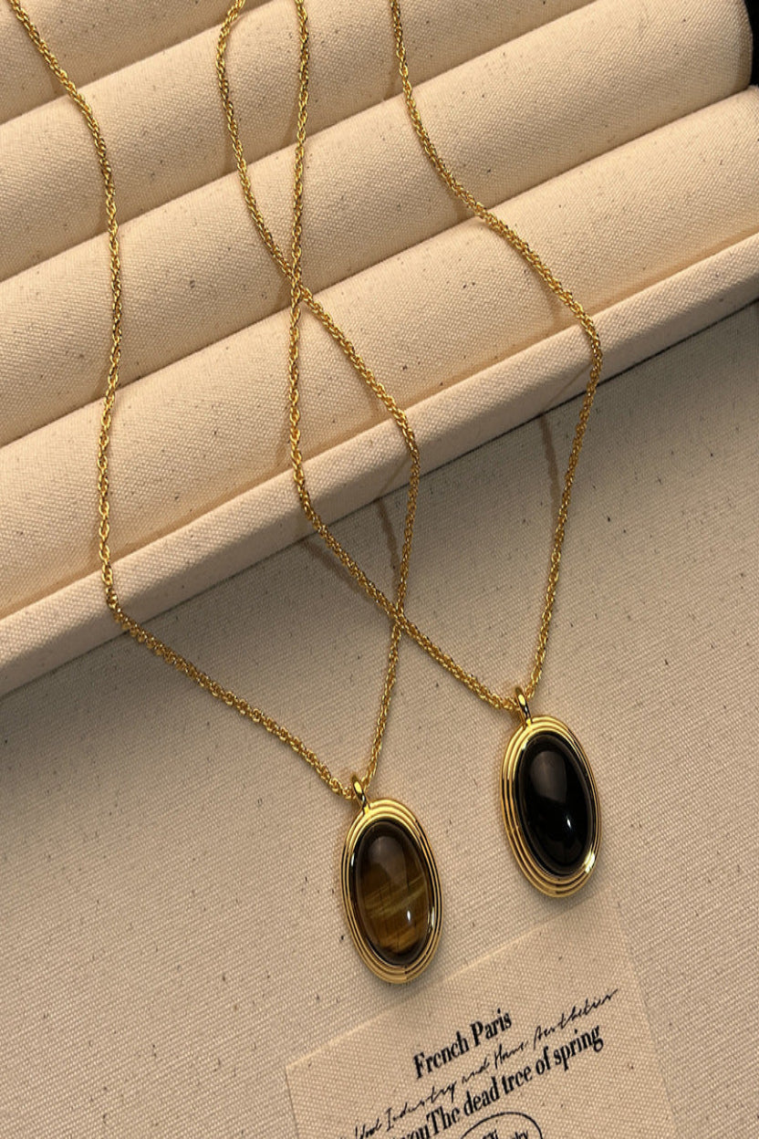 Two gold necklaces with black and brown gemstones on a beige surface.