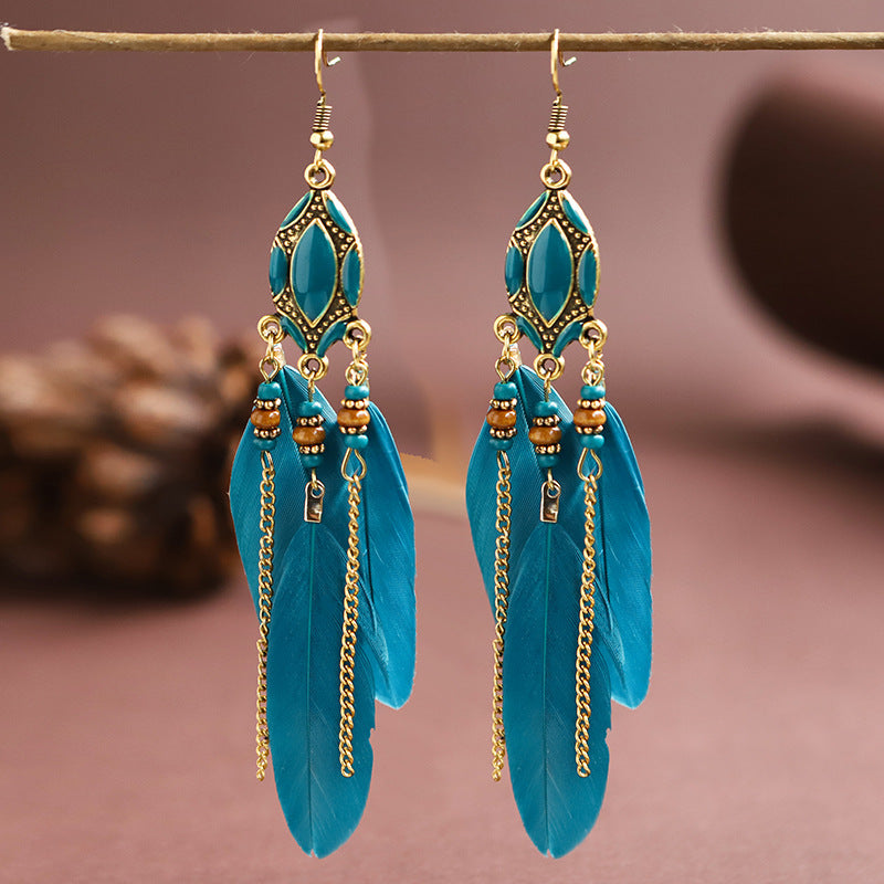 Turquoise feather earrings with gold accents on a brown background from Nested Wisdom