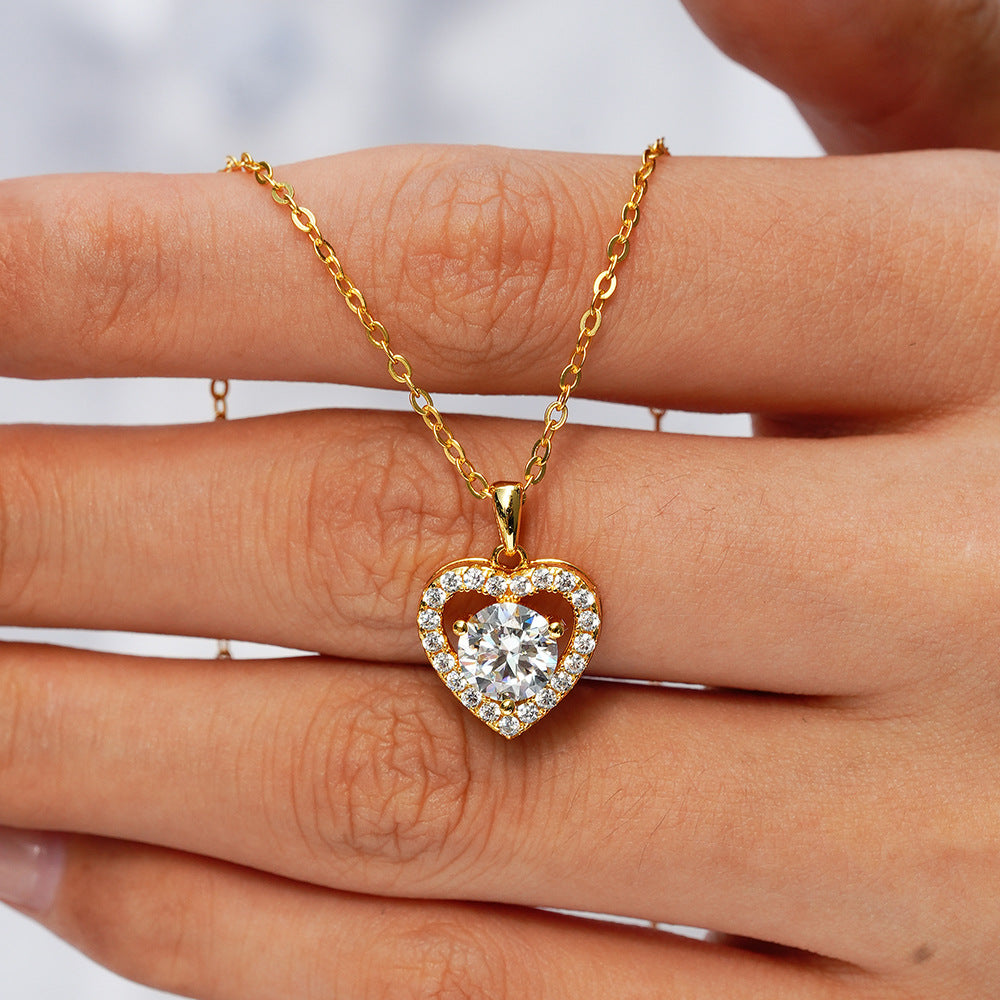 Gold heart-shaped necklace with a diamond pendant held between fingers.