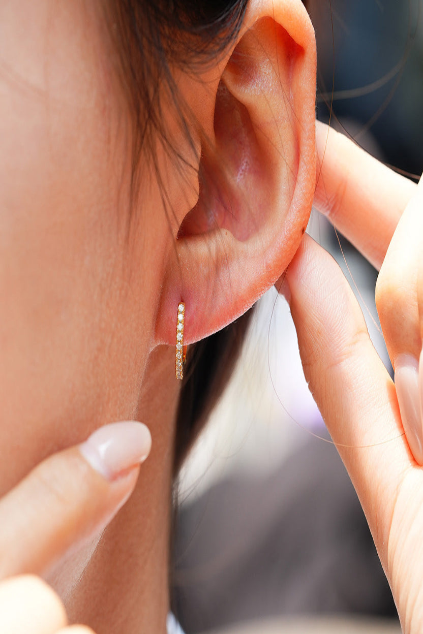 Close-up of an ear wearing a gold hoop earring with a blurred background
