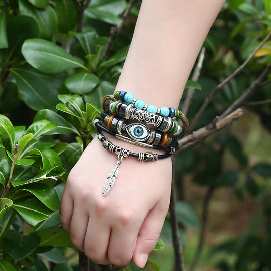 Hand wearing multiple bracelets with green leaves in the background
