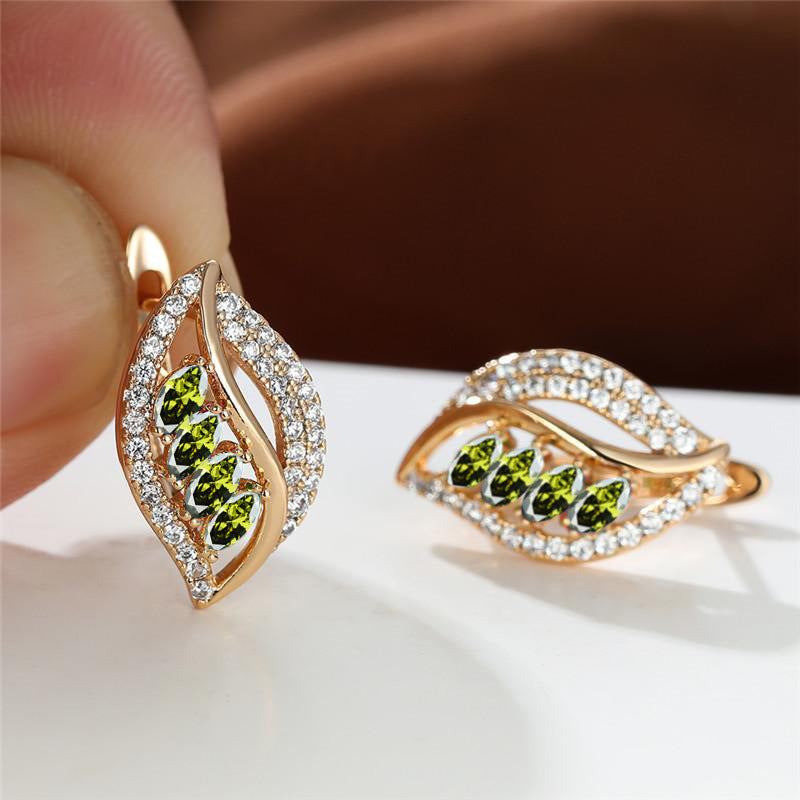 Gold earrings with green gemstones held by a hand on a white surface.
