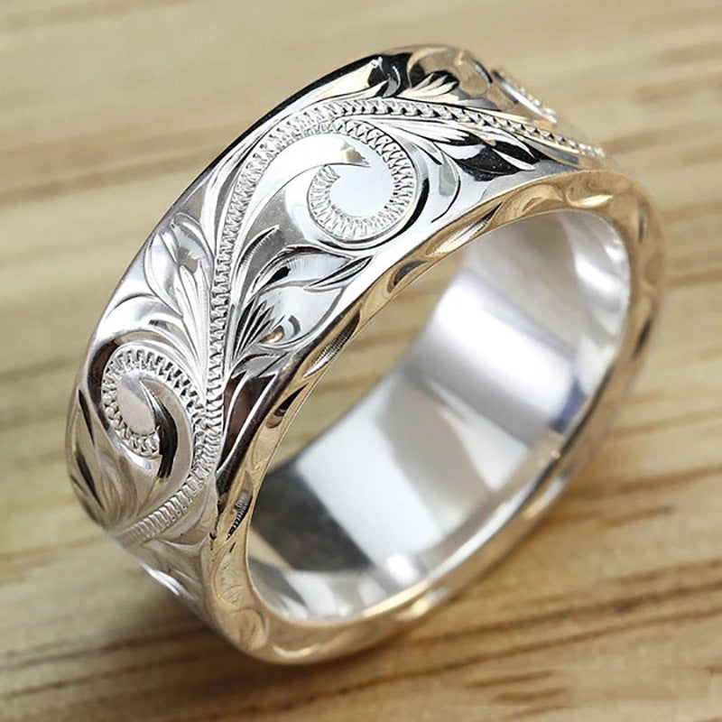 Silver ring with intricate gold engraving on a wooden surface