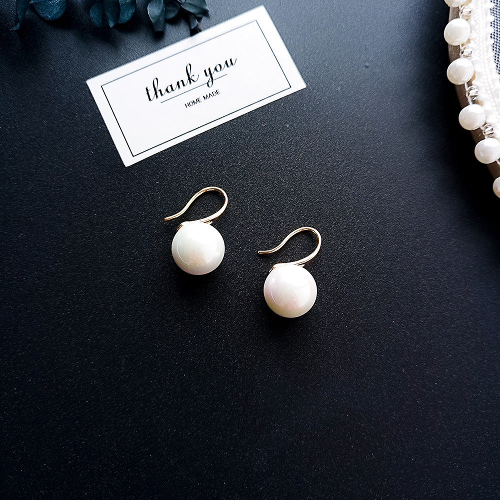 Pearl earrings on a black surface with a 'thank you' card.