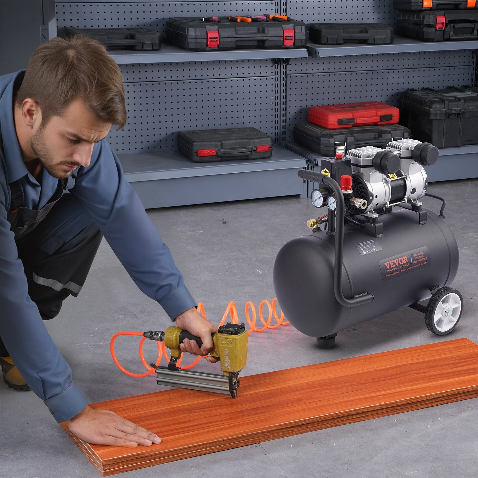 Man using a nail gun on wooden flooring with an air compressor in a workshop setting.