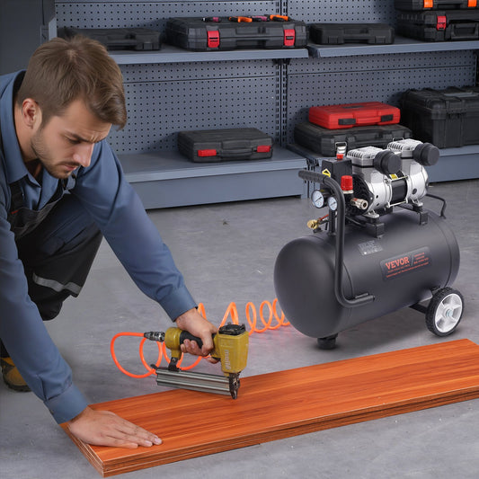 Man using a nail gun on wooden flooring with an air compressor in a workshop setting.