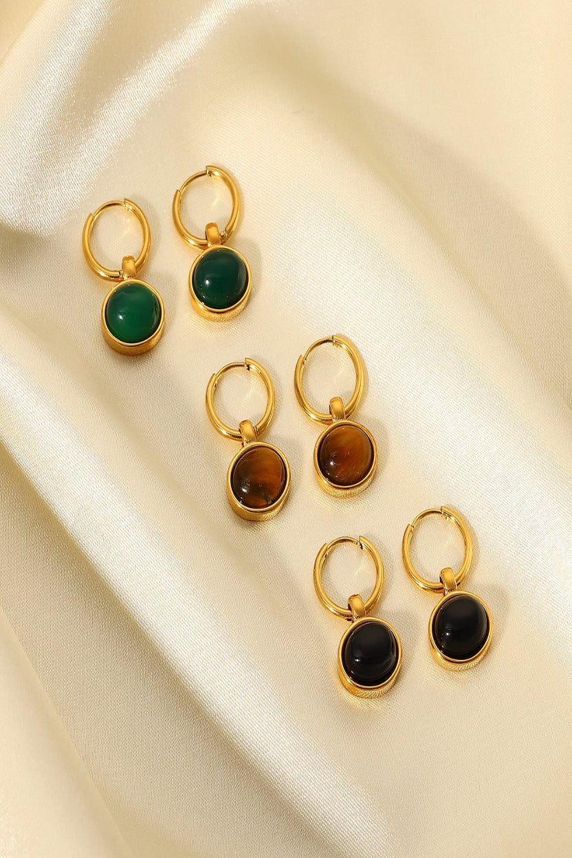 Set of gold earrings with green, brown, and black gemstones on a beige fabric background