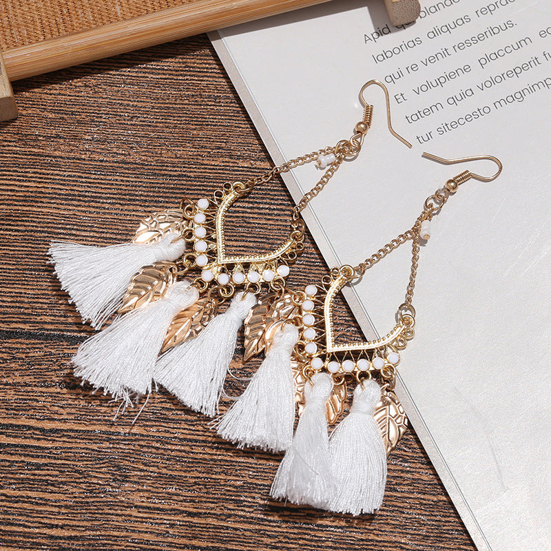 Gold earrings with white tassels on a wooden surface