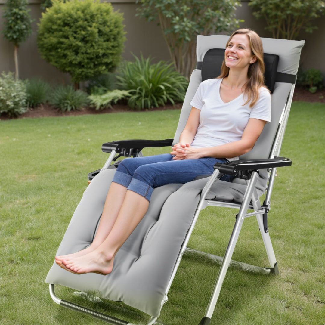 Woman sitting in a gray reclining chair on a grassy area with plants in the background