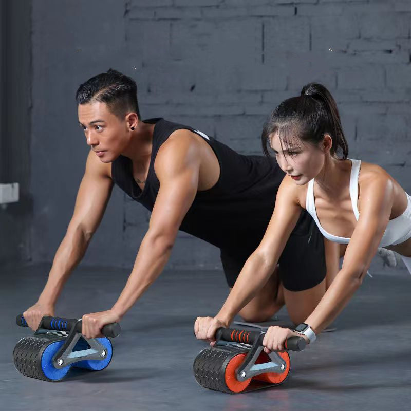 Two people using foam rollers on a gray floor with a brick wall background