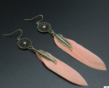 Feather-shaped earrings with pink leaves and gold accents on a dark background