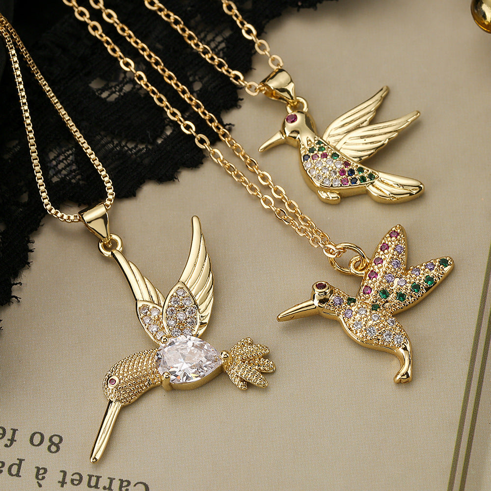 Gold hummingbird pendants with gemstones on gold chains against a textured background.