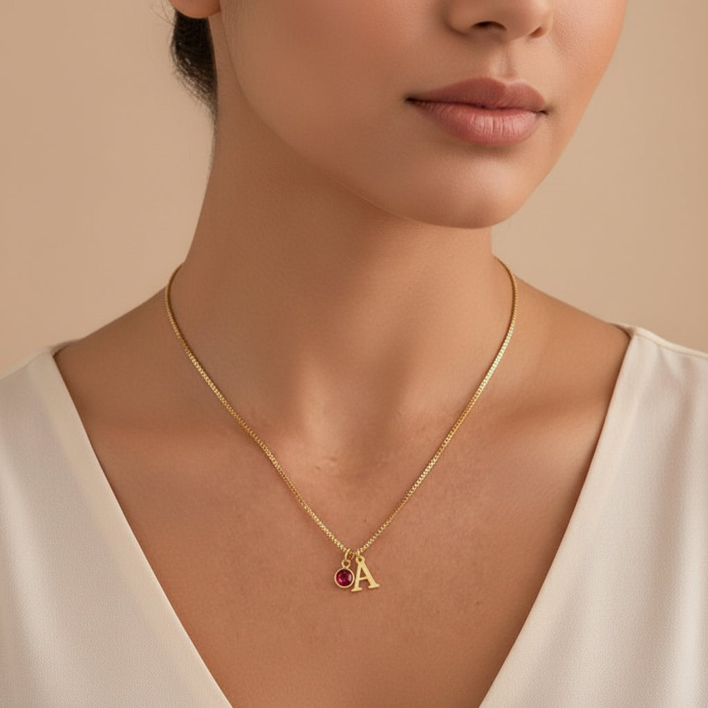 Gold necklace with a red gemstone and letter 'A' pendant on a skin-toned background