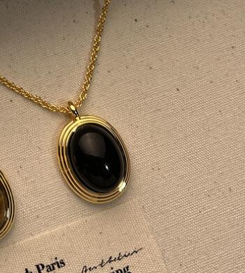 Gold necklace with a black pendant on a beige fabric background