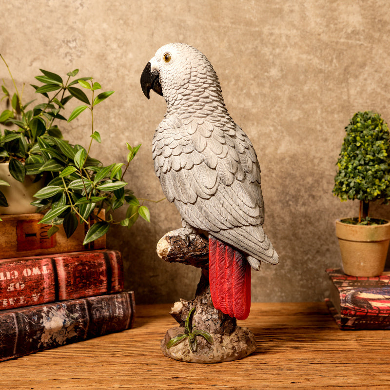 Statue of a parrot on a branch with books and plants in the background