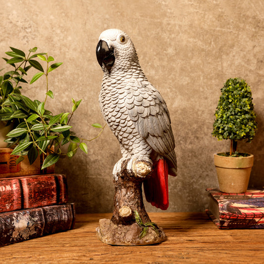 Gray parrot statue on a branch with decorative books and plants in the background