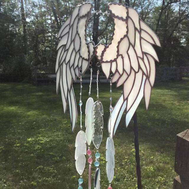 Decorative angel wing wind chime with feathers on a grassy background