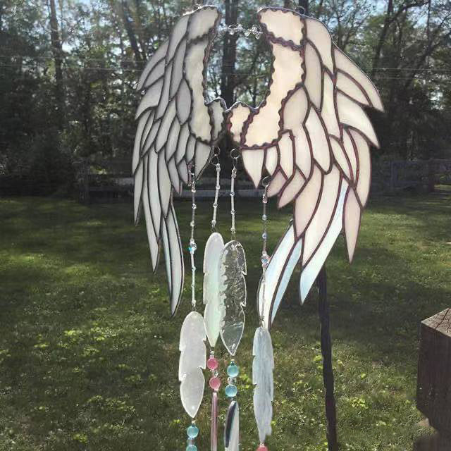 Decorative angel wing wind chime with feathers on a grassy background