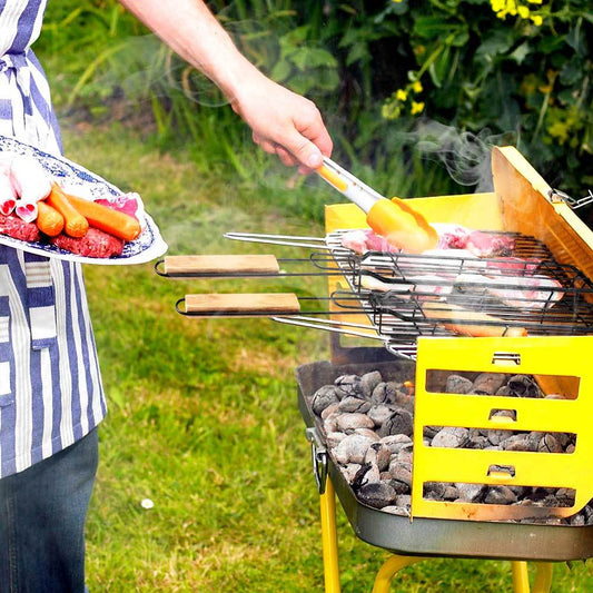 Person grilling outdoors with a yellow grill and vegetables on a plate.
