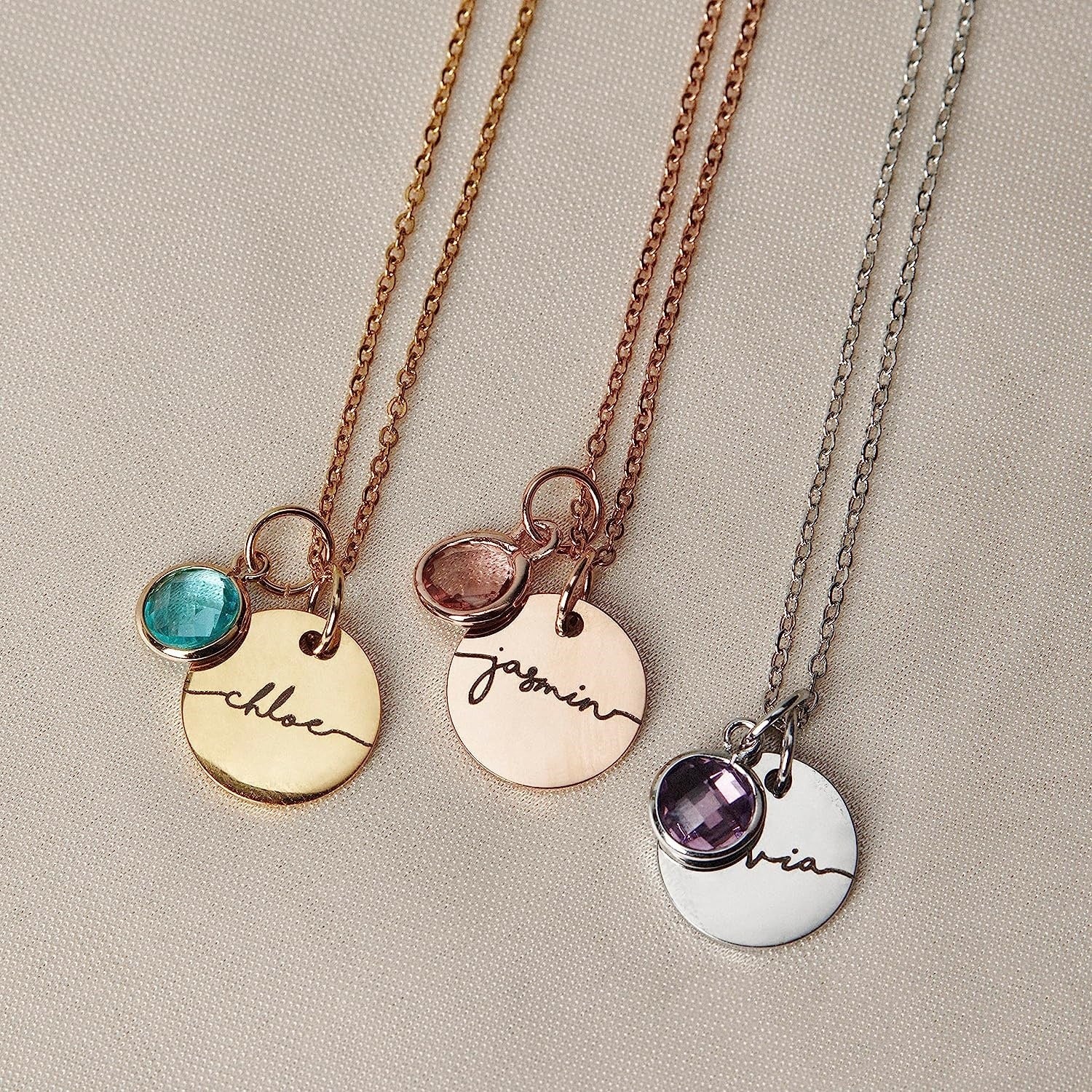 Three necklaces with engraved names and gemstones on a neutral background