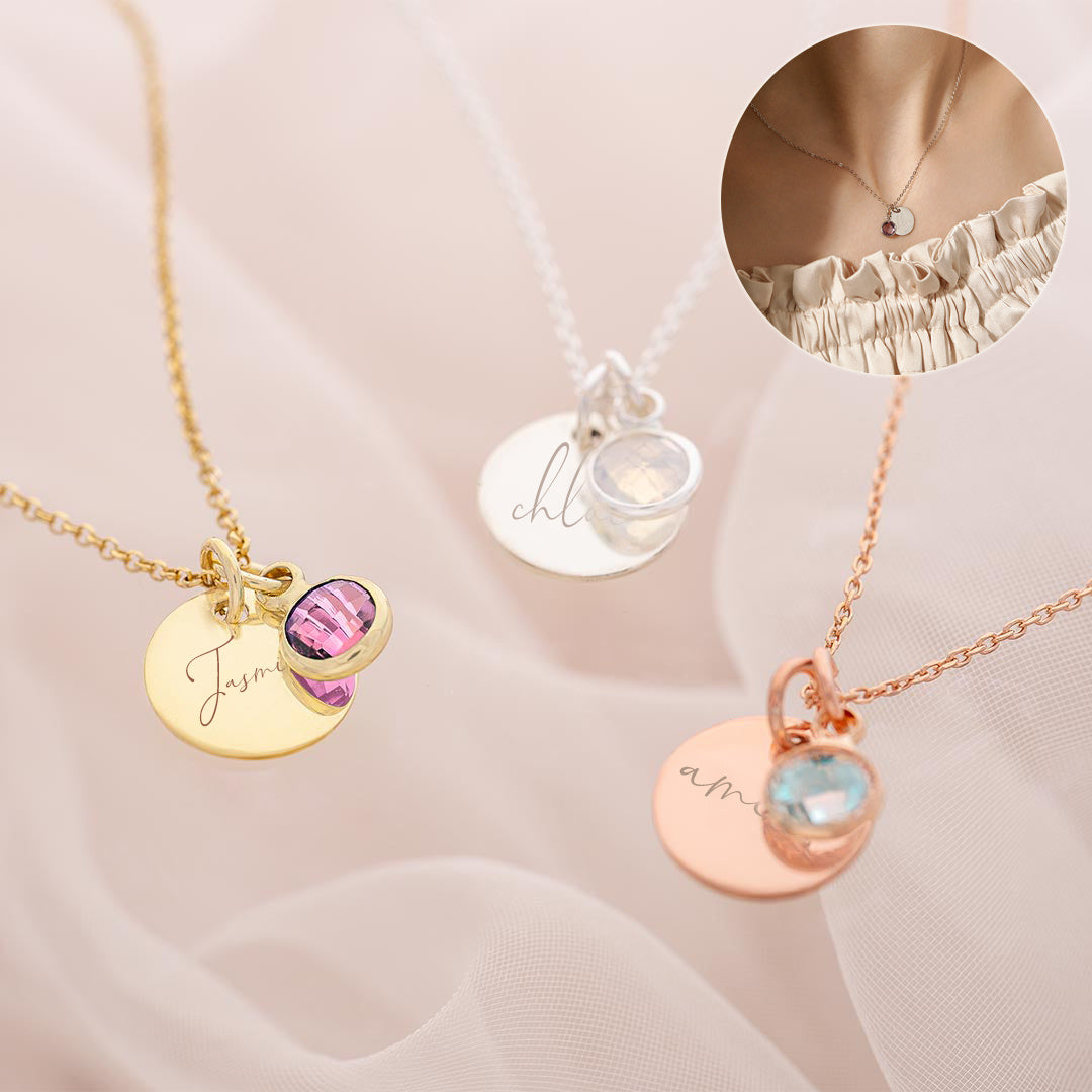Three necklaces with engraved names and gemstones on a soft pink background