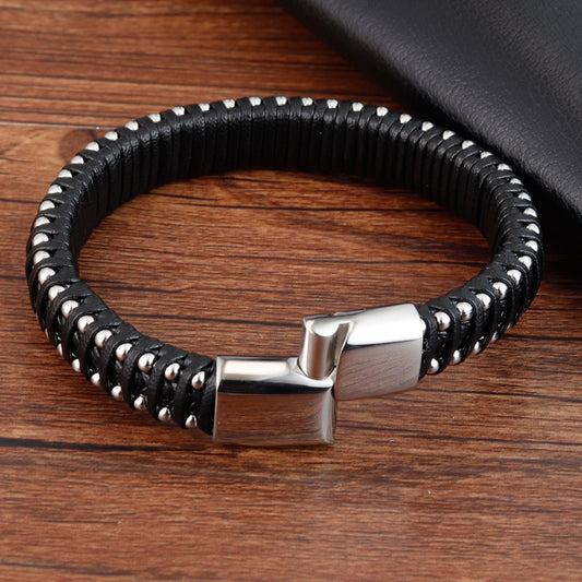 Black braided leather bracelet with silver clasp on a wooden surface