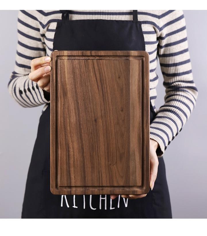 Person holding a wooden cutting board with 'KITCHEN' text on a plain background