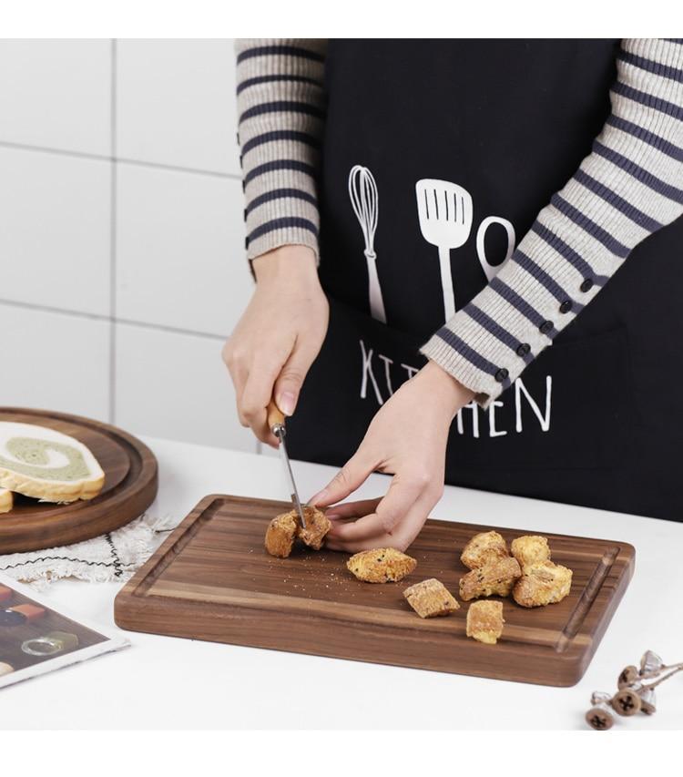 Person cutting food on a wooden board with a kitchen apron in the background