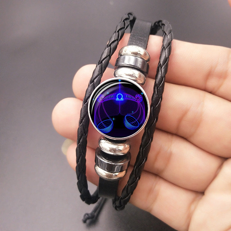 Black braided bracelet with a blue and purple circular design held in a hand against a gray background