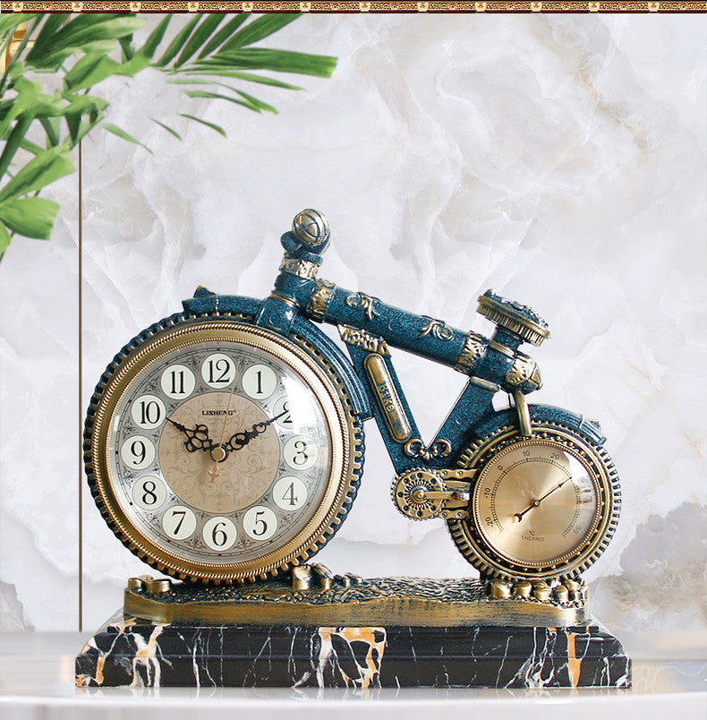 Decorative clock shaped like a blue bicycle on a marble base with green leaves in the background