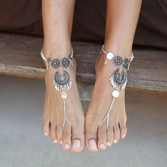 Silver anklets with decorative elements on feet against a neutral background