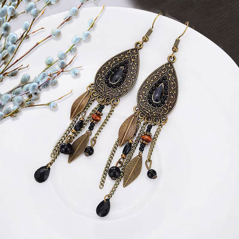 Bohemian-Tribal-Fringe-Earrings-Ornate earrings with black stones and gold accents on a white surface with decorative branches.