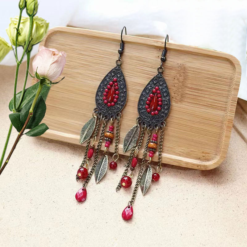 Bohemian-Tribal-Fringe-Earrings- red Pair of decorative earrings with red beads and leaf details on a wooden tray.