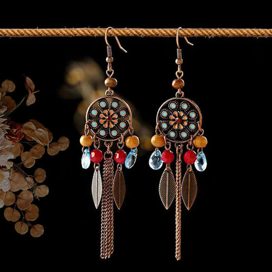 Pair of decorative earrings with beads and feathers on a dark background