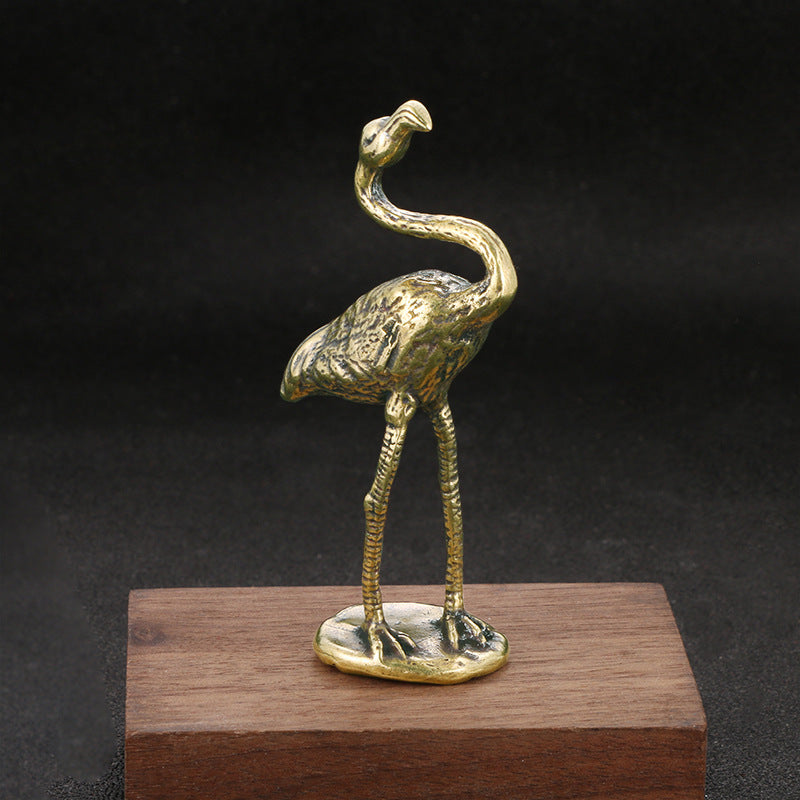 Brass flamingo sculpture on a wooden base against a dark background