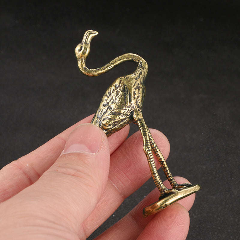 Gold flamingo figurine held in a hand against a dark background