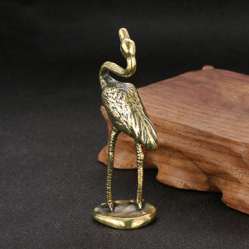 Bronze heron figurine on a dark surface with a wooden block in the background